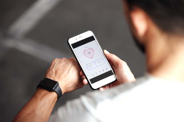 Guy wearing fitness tracker on arm and reading data about heart rate, body temperature and blood pressure on a phone screen.